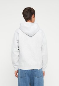 Gray hoodie with a large, adjustable hood, soft texture, relaxed fit, and ribbed cuffs, paired with blue baggy jeans. Back view.