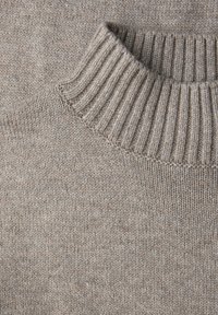 Pull beige doux en tricot avec un col montant côtelé épais, montrant la texture détaillée du tissu et les coutures.