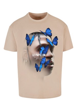 Bēšas krāsas T-krekls ar attēlu, kurā redzama seja, pārklāta ar ziliem tauriņiem un uzrakstu "LE PAPILLON" baltā krāsā, demonstrējot gludu tekstūru.