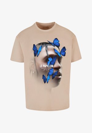 T-shirt beige avec un graphique d'un visage surmonté de papillons bleus et le texte "LE PAPILLON" en blanc, présentant une texture lisse.