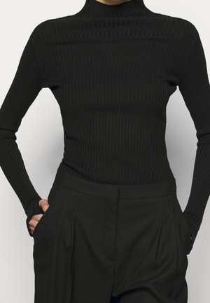 Sort ribbet rullekravesweater med lange ærmer, tætsiddende silhuet, tekstureret stof, parret med højtaljede sorte bukser.
