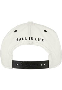 White baseball cap with black embroidered text "BALL IS LIFE" on the back. Features a black adjustable strap and textured fabric.