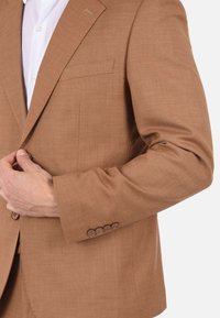 Blazer marrone con texture, colletto a revers e una tasca sul petto. Caratterizzato da chiusura a cinque bottoni sui polsini e una finitura in tessuto liscia.