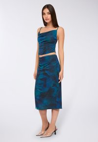 Dwuczęściowy zestaw składający się z obcisłego, bezrękawnikowego topu oraz spódnicy o średniej długości, wykonany z jedwabistego materiału w ciemnoniebieskim kolorze z zielonymi abstrakcyjnymi wzorami.