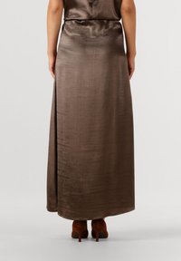 Bruine satijnen maxi rok met een gladde textuur, een hoge taille en een zijsplit, gecombineerd met diep bruin hoge hakken.