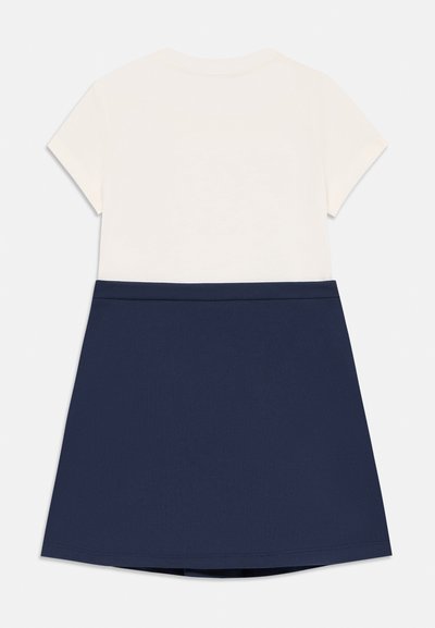 Falda azul marino con una blusa crema, con mangas cortas y escote redondo. Textura suave, diseño sencillo y sin patrones visibles.