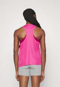 Top in cotone fucsia con scollatura a racerback e texture in rete, abbinato a pantaloni shorts grigi chiari. Presenta un design minimalista con logo sul colletto.
