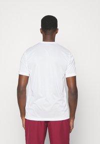 Camiseta blanca de manga corta con cuello redondo y textura suave, combinada con pantalones cortos color burdeos, que muestra un diseño simple y limpio.