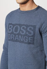 Sudadera de algodón azul para hombre con un logo texturizado en azul oscuro "BOSS ORANGE" en el pecho, con cuello redondo y mangas raglán.