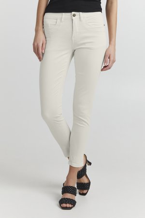 Helle beige Skinny Jeans mit glatter Textur, ausgestattet mit vorderen Taschen und einem einzigen Knopfverschluss, kombiniert mit schwarzen geflochtenen High-Heels.