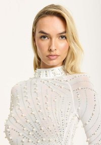 White sheer dress adorned with scattered pearls and rhinestones in a swirling pattern. High collar, long sleeves, and fitted silhouette.