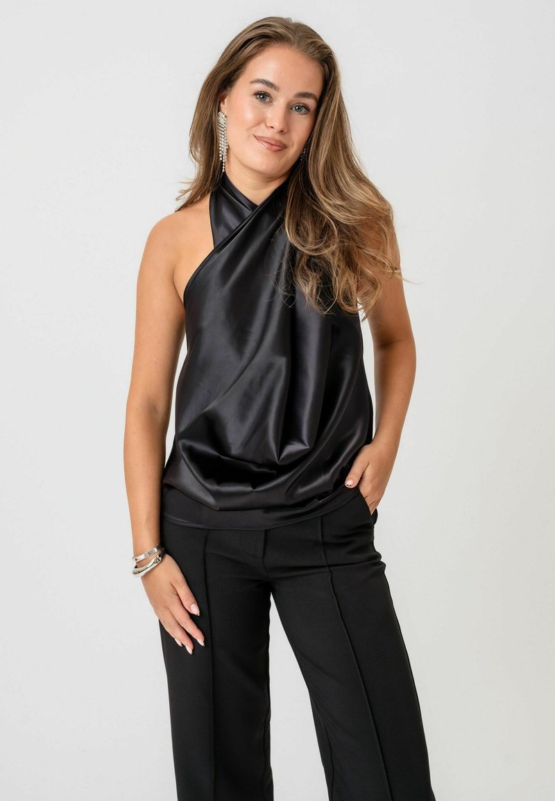 Fekete selyem halter-top drapírozott designnal, sima textúrával. Tailored fekete nadrággal párosítva, amely tiszta sziluettekben mutatkozik meg.