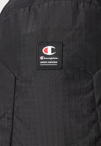 Fekete, steppelt nylon anyag, melyen egy kis Champion logófelvarró látható az "AUTHENTIC ATHLETICWEAR" szöveggel. Hálós mintázattal rendelkezik.
