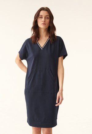 Rochie bleumarin dintr-un material moale, cu decolteu în V, mâneci scurte, buzunar frontal și detalii cu dungi albe la decolteu.