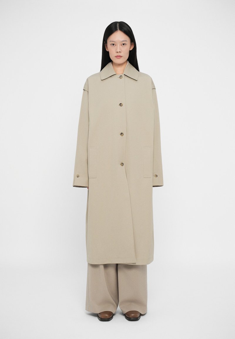 Μπεζ μακριά παλτό με κολάρο, μακριά μανίκια και κ�λείσιμο με κουμπιά μπροστά. Περιλαμβάνει πλαϊνές τσέπες και καθαρό, μινιμαλιστικό σχέδιο.