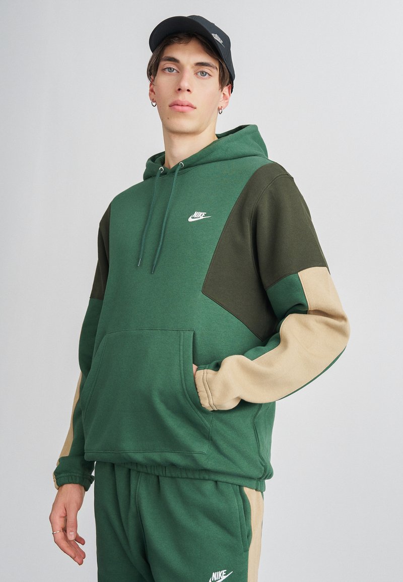 Vihreä ja beige huppari, jossa on kengurupussi, Nike-logo rinnassa ja värikohdistetut hihat. Pehmeä kangas, rento istuvuus.