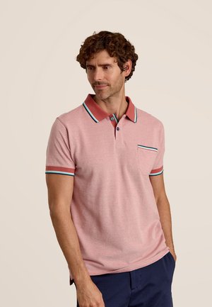 Polo shirt rose clair avec un col rouge, des finitions bleues et vertes sur les manches et la poche. Manches courtes, texture douce et patte de boutonnage.