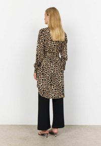 Leopardmönstrad skjortklänning med insvängd midja, långa ärmar och rundad nederkant, tillsammans med svarta vida byxor och mönstrade klackar med öppen tå.