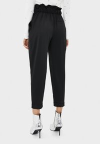 Schwarze, lässige Hose mit gerüschtem Taillenbund, seitlichen Taschen und umgeschlagenen Säumen, kombiniert mit glänzenden silbernen Knöchelschuhen.