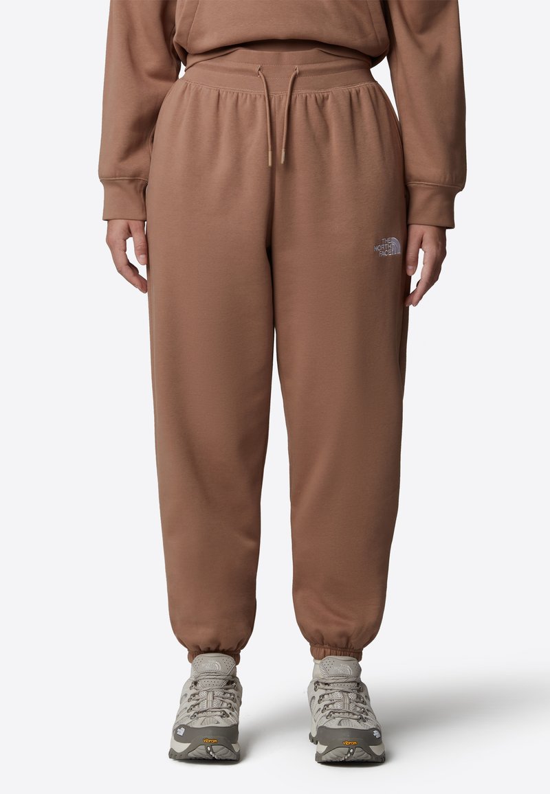 Bruna träningsbyxor med elastisk midja och muddar, med en diskret logotyp på låret. Tyget verkar mjukt med en slät yta.