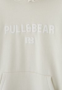 Felpa beige con testo in rilievo bianco "PULL&BEAR" e logo "PB" sopra una tasca frontale.