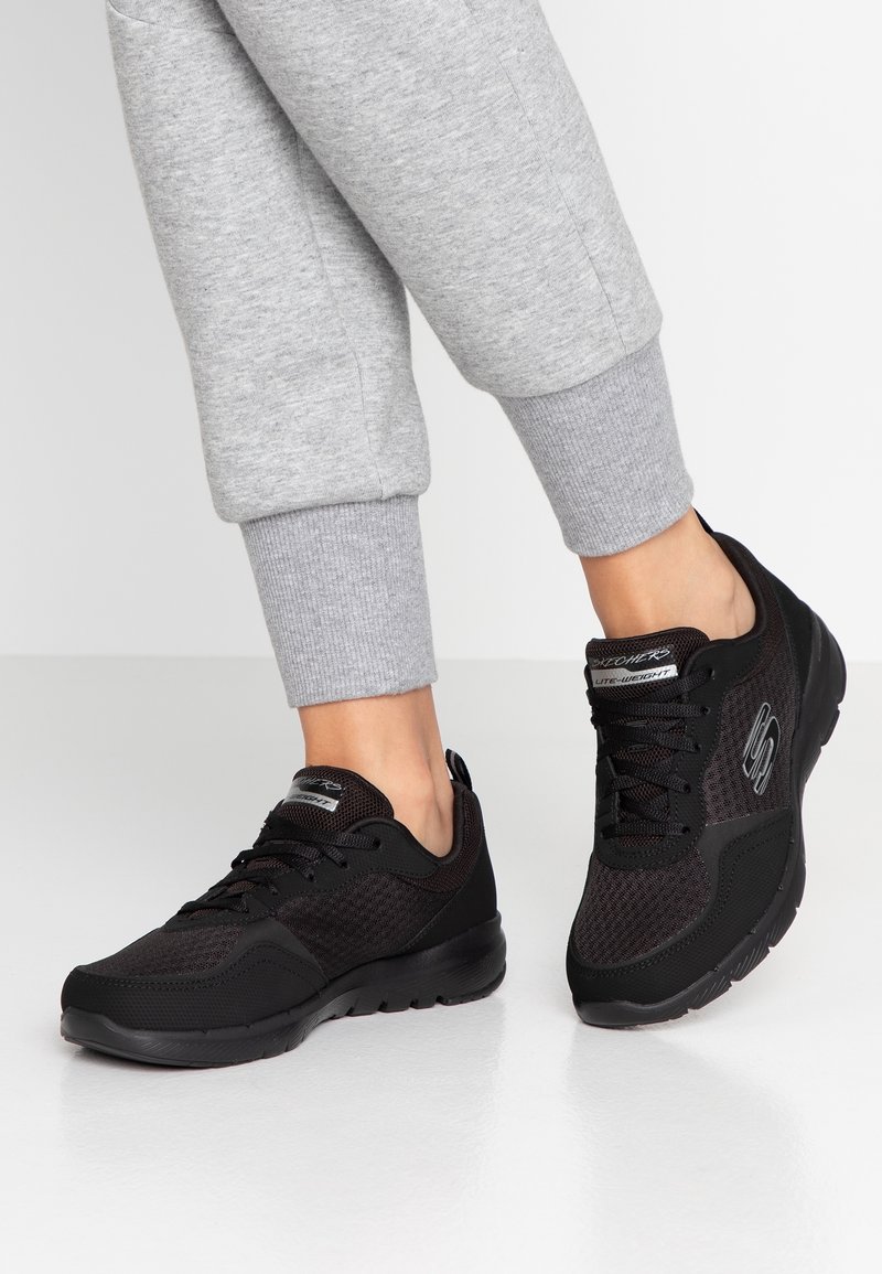 Svarta löparskor i mesh och syntetiska material, med rund tå, snördesign och logotypdetalj på sidan.