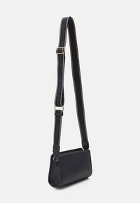 Borsa a tracolla in pelle nera con forma rettangolare piatta. Presenta una cintura larga con "TOMMY HILFIGER" in accenti blu e oro.