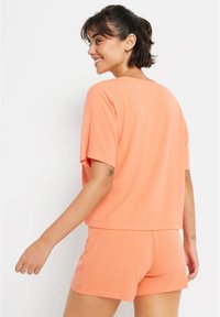 Kortärmad, löst sittande topp och matchande shorts i ribbat, ljusorange tyg. Har en rund halsringning och en avslappnad silhuett.