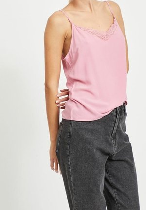 Camisola in satin rosa con pizzo lungo il colletto, dotata di sottili spalline. Abbinata a jeans grigi scuri a vita alta.