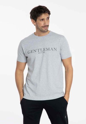 T-shirt gris à manches courtes en mélange de coton, avec un imprimé à l'avant "GENTLEMAN EST.90" en texte gris foncé. Coupe décontractée avec col rond.