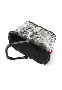 Sac en toile noir et blanc avec un motif floral, présentant une forme courbée, des poignées noires et une poche intérieure zippée.