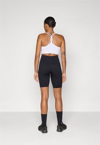 Witte sportbh met kruislings straps, gecombineerd met hoge zwarte fietsshorts. Zwarte sokken en schoenen maken de outfit compleet.
