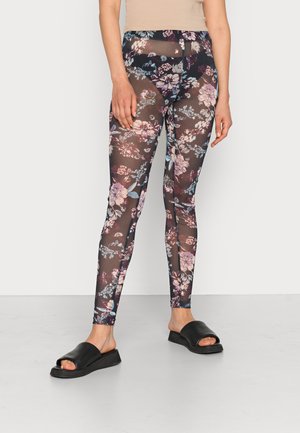 Leggings transparent com estampado floral em tons escuros, com flores roxas e azuis; combinados com sandálias deslizantes pretas apresentando um design plano.