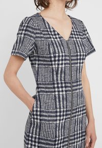 Robe à motifs bleu marine et blanc avec manches courtes, col en V et fermeture éclair à l'avant. Présente un design pied-de-poule texturé et des poches latérales.