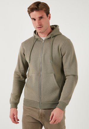 Olivovo zelená mikina na zips vyrobená z mäkkej tkaniny, s kapucňou na stiahnutie, prednými vreckami a rebrovanými manžetami a spodným lemom.