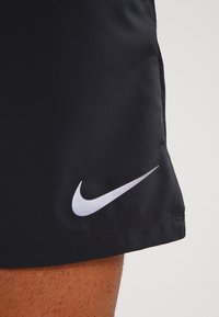Pantalones cortos Nike negros con una textura suave, un logo blanco en la parte inferior izquierda y un diseño de dobladillo recto.