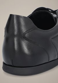 Czarne skórzane buty z gładką fakturą, zaokrąglonym obcasem i subtelnymi akcentami przeszyć. Projekt jest minimalistyczny i opływowy.