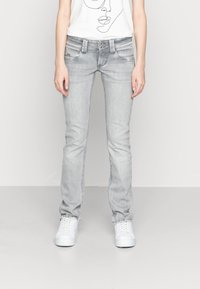 Slim-fit ljusgrå jeans med en blekt tvätt, med fem fickor, metallknappar och vita canvas sneakers.