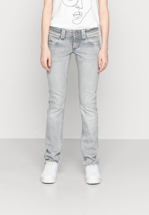 Vaqueros slim-fit de color gris claro con un lavado desgastado, que cuentan con cinco bolsillos, botones de metal y zapatillas de lona blanca.