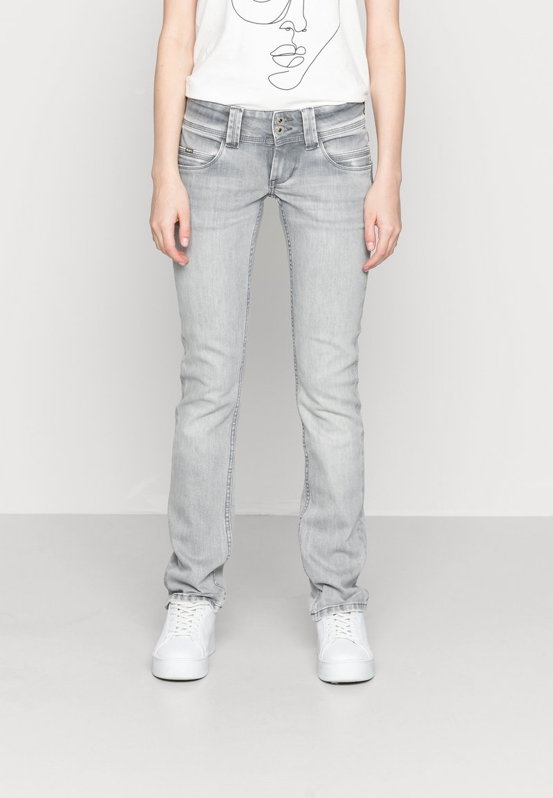 Slim-fit ljusgrå jeans med en blekt tvätt, med fem fickor, metallknappar och vita canvas sneakers.
