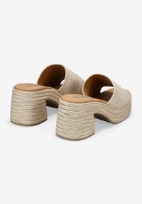 Sandali beige con punta aperta e plateau, caratterizzati da una tomaia intrecciata testurizzata, un tacco arrotondato e un design simile a una corda sulla suola rialzata.