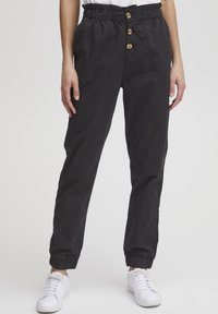Pantalons noirs cintrés avec une taille élastique et trois boutons en bois. Avec des poignets aux chevilles, fabriqués à partir d'un tissu doux et durable.