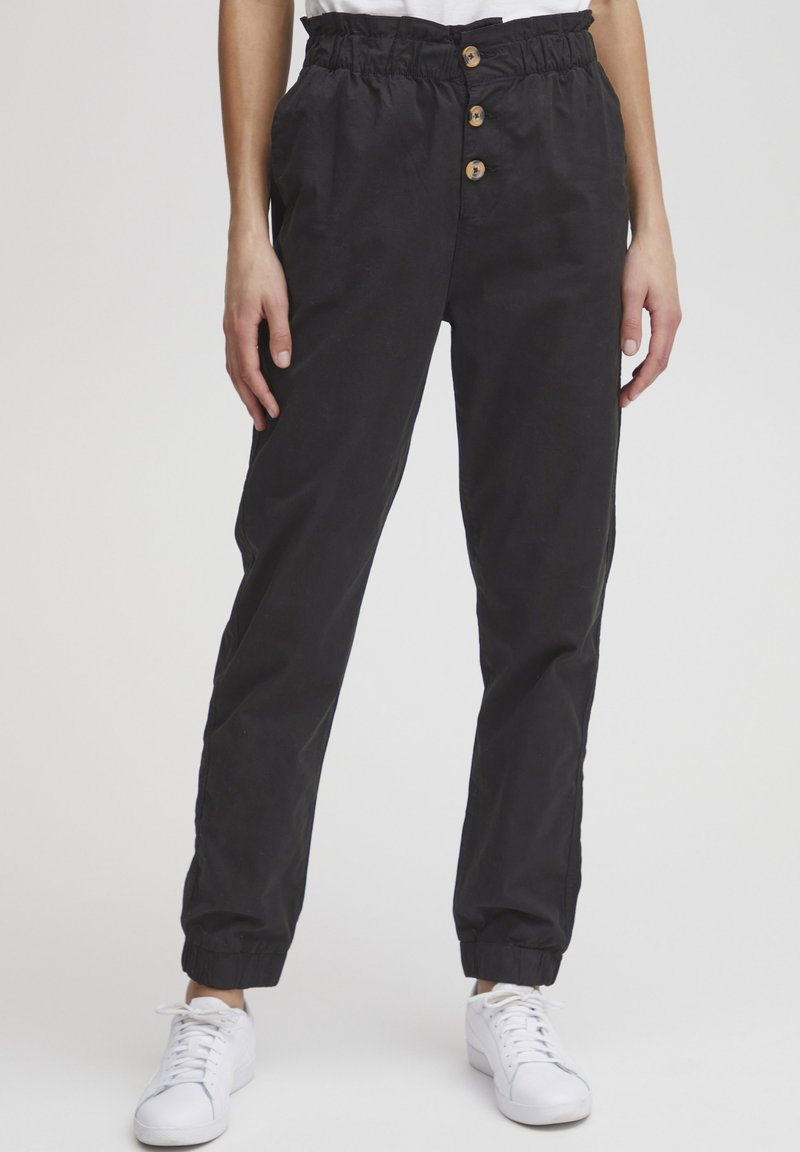 Pantalons noirs cintrés avec une taille élastique et trois boutons en bois. Avec des poignets aux chevilles, fabriqués à partir d'un tissu doux et durable.