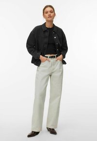 Crna traper jakna preko crnog topa, uparena sa svijetlo bež širokim hlačama i smeđim čizmama s potpeticom, s prednjim džepovima i remenom.