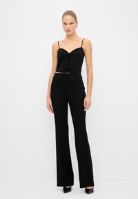 Top negro cortado con tirantes finos y escote corazón, combinado con pantalones de cintura alta y pierna acampanada negros. Tela suave, diseño elegante.