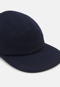 Căciulă bleu marin cu un material texturat, vizor curbat și detalii cusute. Prezintă un design cu șase panele și o coroană structurală.