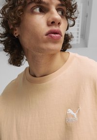 Lyserød kortærmet t-shirt lavet af blødt bomuld, med et lille hvidt broderet Puma-logo på brystet.