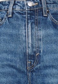 Modré denimové džíny s kontrastním oranžovým prošíváním, stříbrným knoflíkem a tradičním pětikapsovým designem. Hladký povrch s mírným odřením.