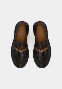 Loafers din piele neagră cu un model de crocodil, accent din lanț de aur și talpă groasă din cauciuc. Interiorul are o finisare maro.