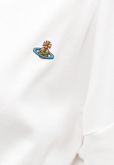 Biely rebrovaný textil s malým vyšívaným logom, ktoré zobrazuje zlatú guľu s modrým prsteňom a oranžovým krížom na vrchu.